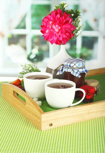 Cups of tea with flower and jam on wooden tray on table in room — Stock Photo, Image