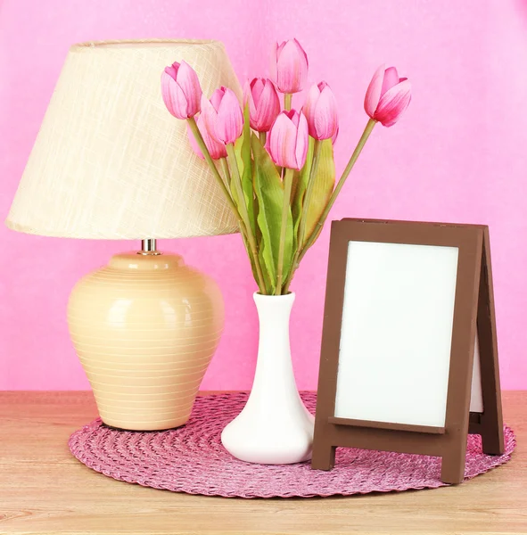 Marco de fotos marrón y lámpara sobre mesa de madera sobre fondo de pared rosa — Foto de Stock