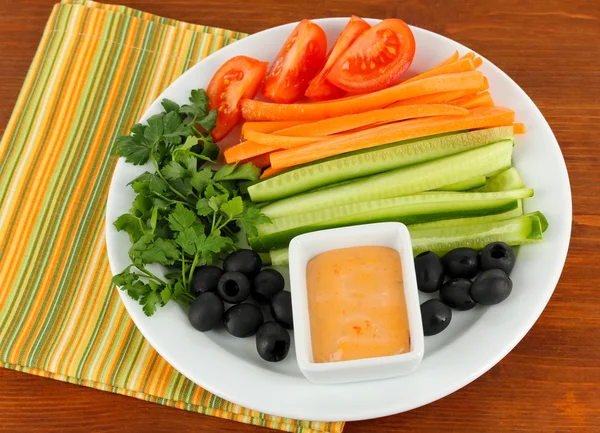 Diverse råa grönsaker pinnar i plattan på träbord närbild — Stockfoto