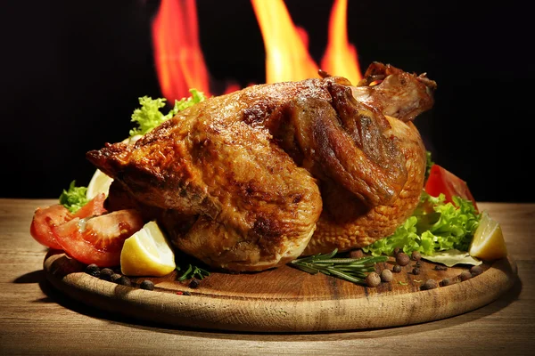 Целый жареный цыпленок с овощами на тарелке, на фоне пламени — стоковое фото