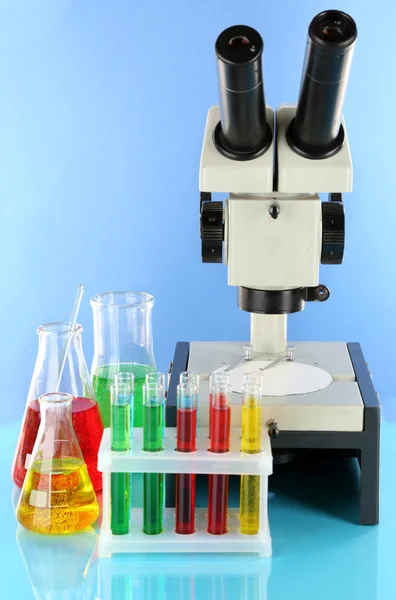 Test tubes with colorful liquids and microscope on blue background — Stock Photo, Image