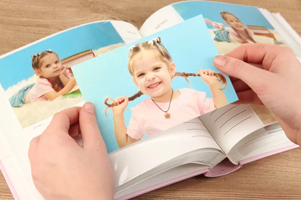 Photos in hands and photo album on wooden table — Stock Photo, Image