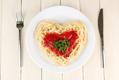 Cooked spaghetti carefully arranged in heart shape and topped with tomato sauce, on wooden background
