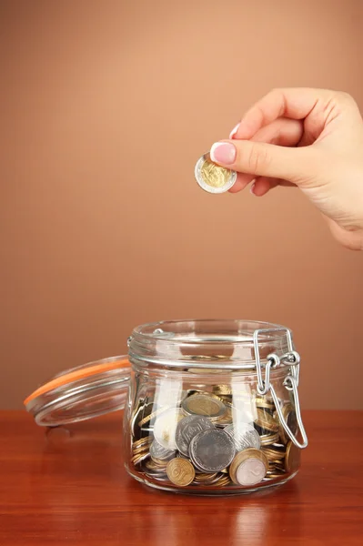 Poupança, mão feminina colocando uma moeda em garrafa de vidro, em fundo de cor — Fotografia de Stock