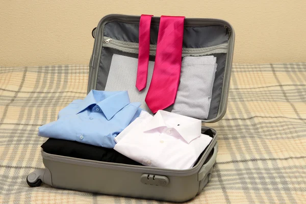 Ανοικτό γκρι βαλίτσα με ενδυμασία σε κρεβάτι — Φωτογραφία Αρχείου