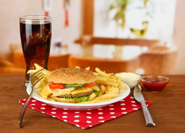 Tasty cheeseburger with fried potatoes and cold drink, on bright background — Stock Photo, Image