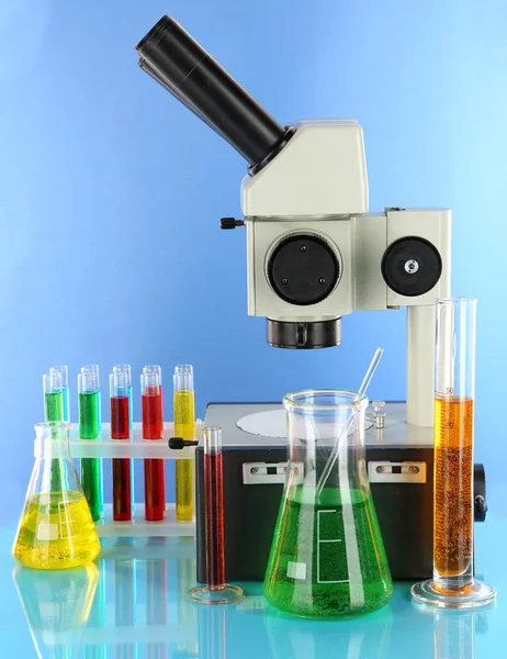 Test tubes with colorful liquids and microscope on blue background — Stock Photo, Image