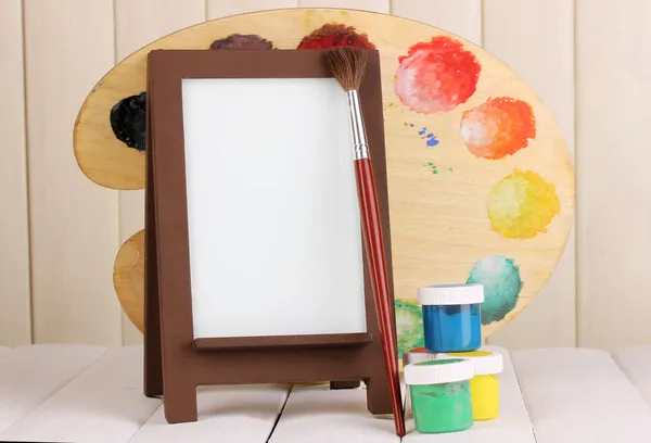Photo frame as easel with artist's tools on wooden background — Stock Photo, Image
