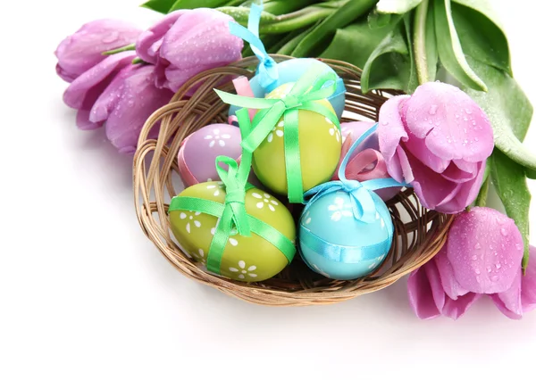 Huevos de Pascua brillantes en cesta y tulipanes, aislados en blanco — Foto de Stock