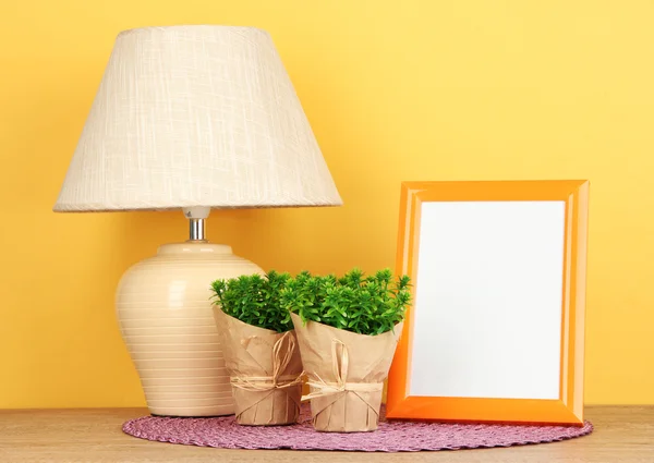 Färgglada fotoram, lampa och blommor på träbord på gul bakgrund — Stockfoto