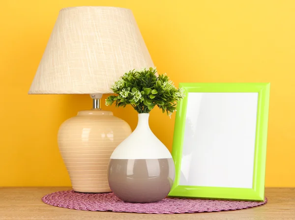 Colorful photo frame, lamp and flowers on wooden table on yellow background — Stock Photo, Image