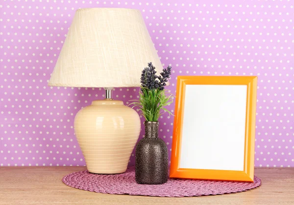 Marco de fotos colorido, lámpara y flores en la mesa de madera sobre fondo de lunares lila —  Fotos de Stock