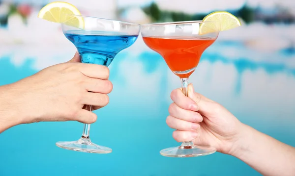 Cocktails in handen van mannen en vrouwen op zwembad achtergrond — Stockfoto