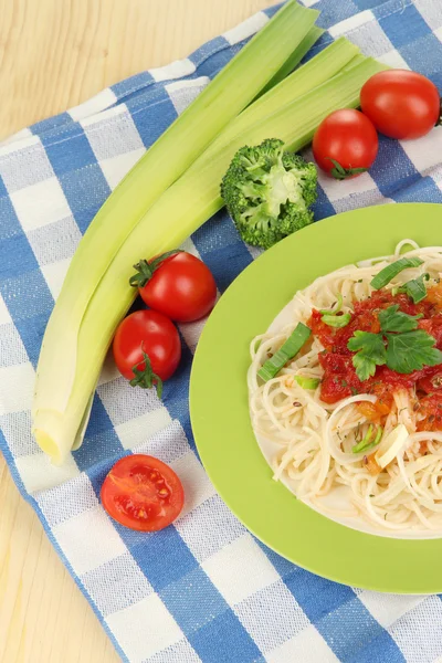 Smakfull spagetti med saus og grønnsaker på tallerkenen på trebord. – stockfoto