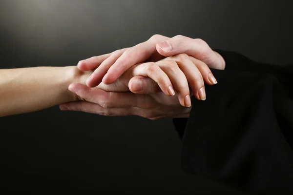 Sacerdote sosteniendo la mano de mujer, sobre fondo negro — Foto de Stock