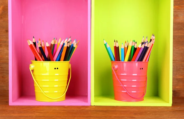 Lápis coloridos em pails em prateleiras sobre fundo de madeira — Fotografia de Stock