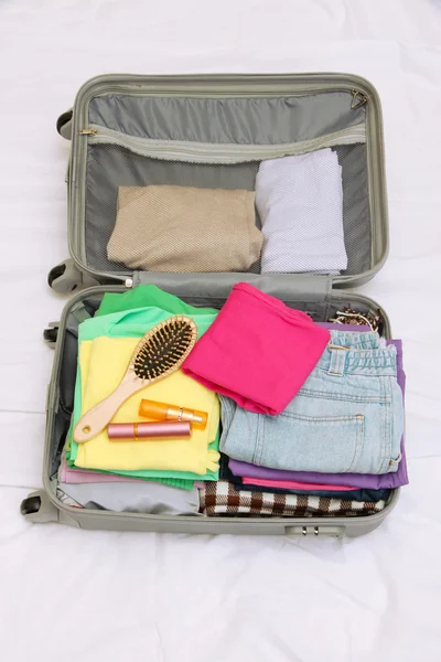 Відкрита сіра валіза з одягом на ліжку — стокове фото