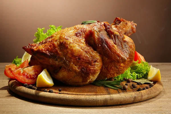 Pollo asado entero con verduras, sobre mesa de madera, sobre fondo marrón — Foto de Stock