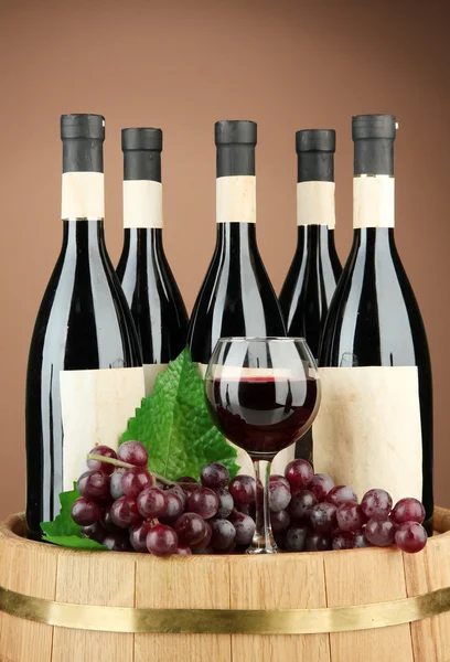 Composição de garrafas de vinho, copos e uva, em barril de madeira, sobre fundo marrom — Fotografia de Stock