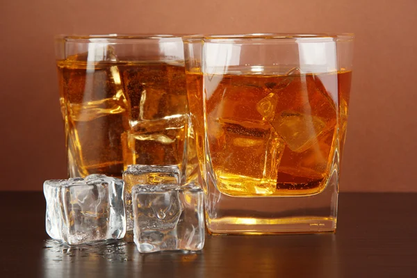 Glazen van whisky en ijs op bruine achtergrond — Stockfoto