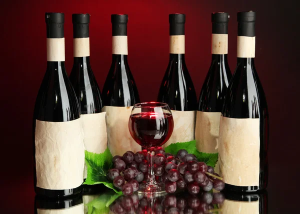 Složení vína lahví, skla a hroznů, na tmavě červeném pozadí — Stock fotografie