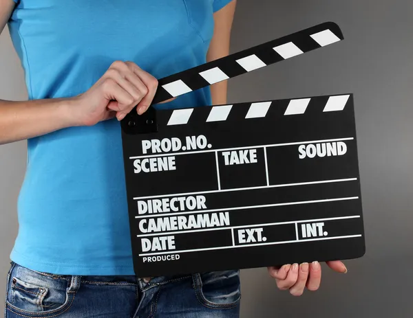 Movie production clapper board in hands on grey background — Stock Photo, Image