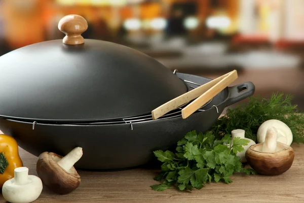 Black wok pan and vegetables on kitchen wooden table, close up — Stock Photo, Image