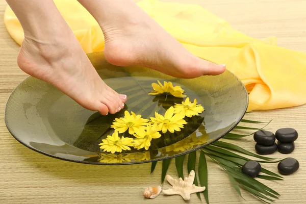 Vrouwelijke voeten in spa kom met water, op bamboe mat — Stockfoto