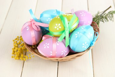 Beyaz ahşap zemin üzerinde sepet ve Mimoza çıtır Paskalya yumurtaları