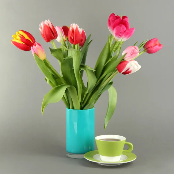 Beautiful tulips in bucket with cup of tea on grey background — Stock Photo, Image