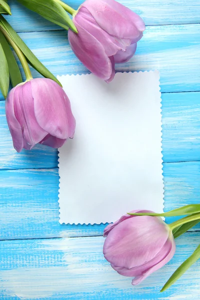 Schöner Strauß lila Tulpen und leere Karte auf blauem Holzhintergrund — Stockfoto