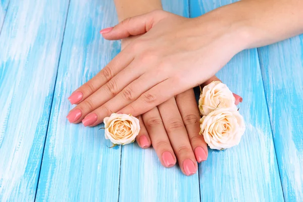 Mãos de mulher com manicure rosa e flores, na cor de fundo de madeira — Fotografia de Stock