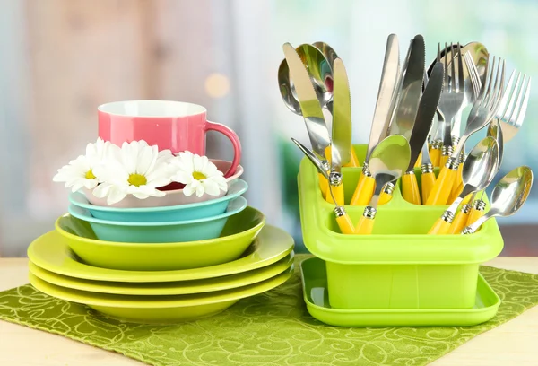 Piatti, forchette, coltelli, cucchiai e altri utensili da cucina su tovagliolo di colore, su sfondo brillante — Foto Stock