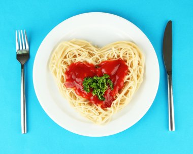 dikkatli bir şekilde kalp şeklinde düzenlenmiş ve renkli arka plan üzerinde domates soslu tepesinde pişmiş spagetti