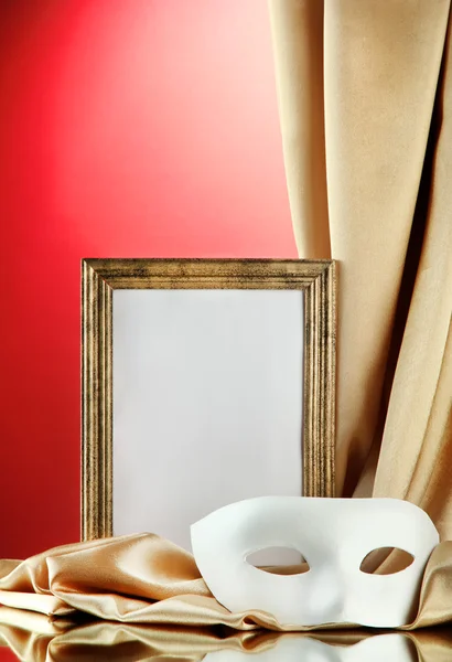 White mask, empty frame and golden silk fabric, on red background — Stock Photo, Image