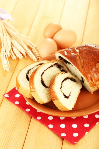 Loaf with poppy seeds on color plate, on wooden background — Stock Photo, Image