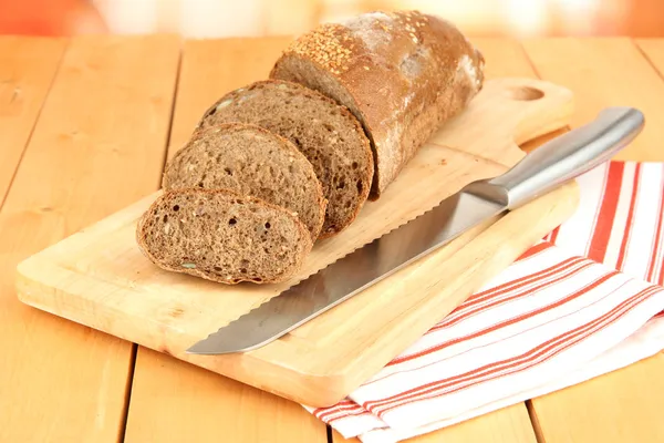 Skivat bröd med sesamfrön och kniv på skärbräda på träbord närbild — Stockfoto