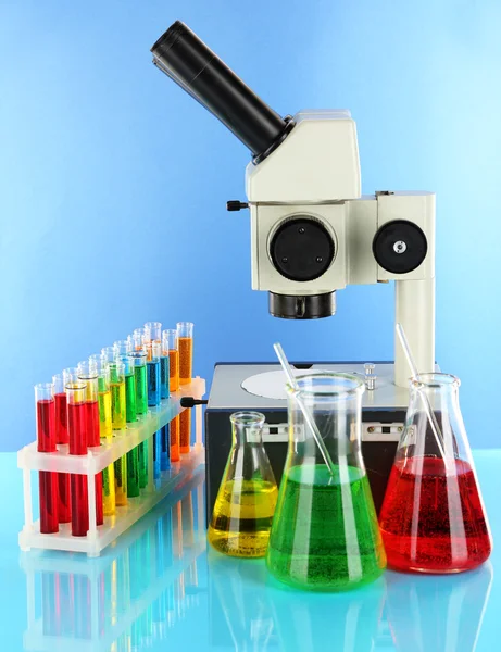 Test tubes with colorful liquids and microscope on blue background — Stock Photo, Image