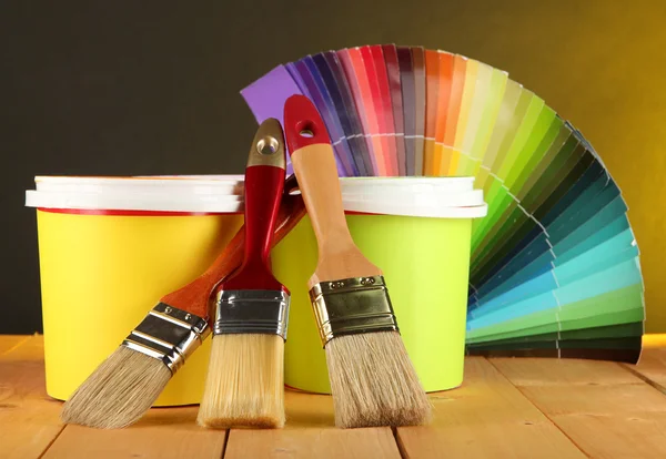 Panelas de pintura, pincéis e amostras coloridas sobre mesa de madeira sobre fundo amarelo escuro — Fotografia de Stock