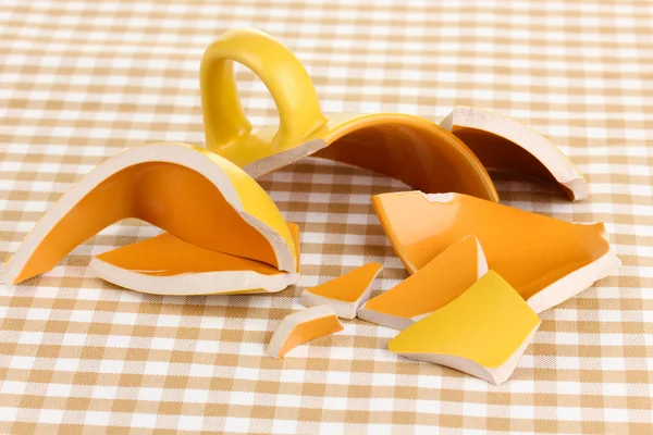 Gelbe zerbrochene Tasse auf Tisch auf kariertem Hintergrund — Stockfoto