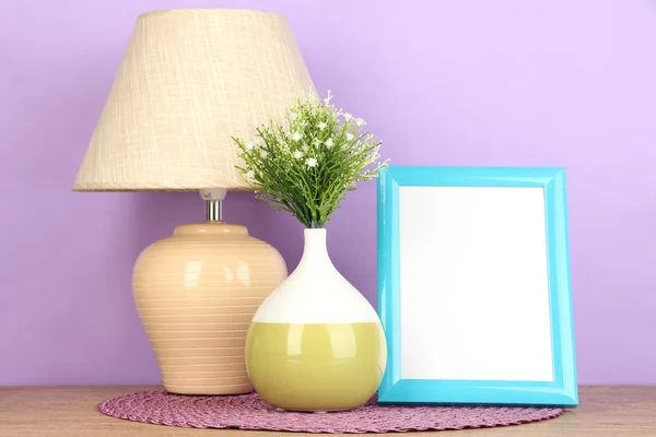 Marco de fotos colorido, lámpara y flores en la mesa de madera sobre fondo lila —  Fotos de Stock