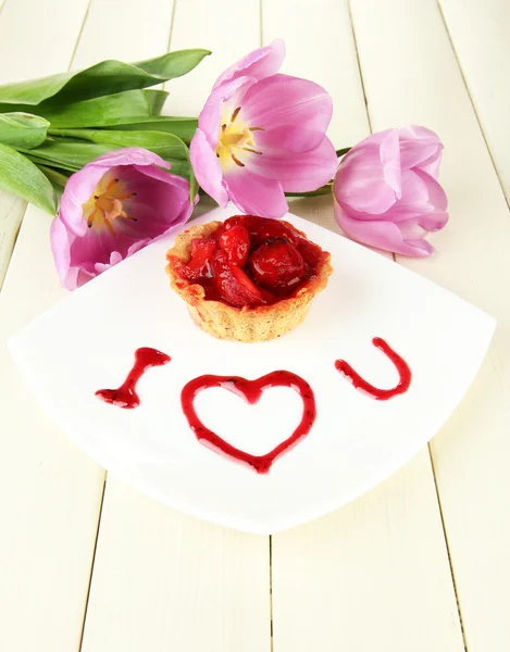 Söt tårta med jordgubbar och sås på plattan, på trä bakgrund — Stockfoto