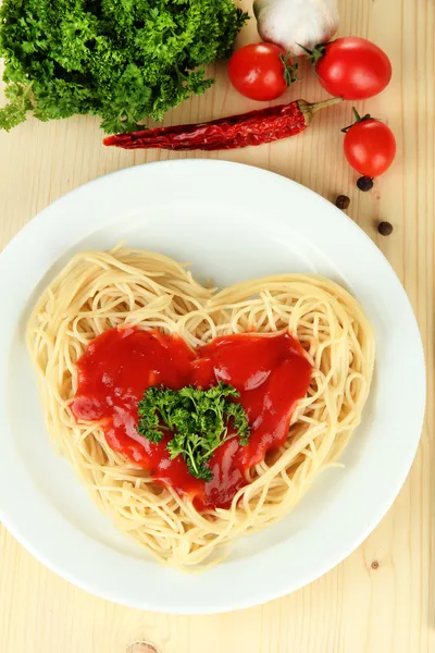 Spaghettis cuits soigneusement disposés en forme de coeur et garnis de sauce tomate, sur fond de bois — Photo