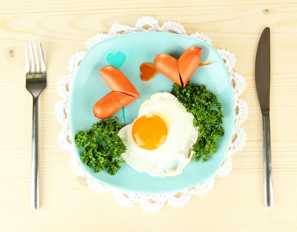 Sausages in form of hearts, scrambled eggs and parsley, on color plate, on wooden background — Stok fotoğraf