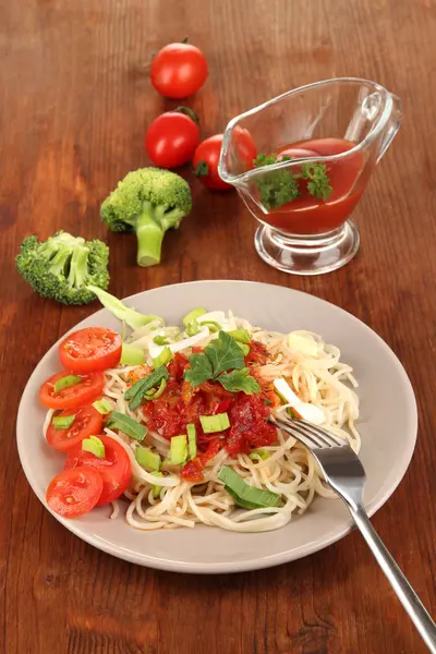 Smaczne spaghetti z sosem i warzywami na tabliczce na drewniany stół szczegół — Zdjęcie stockowe