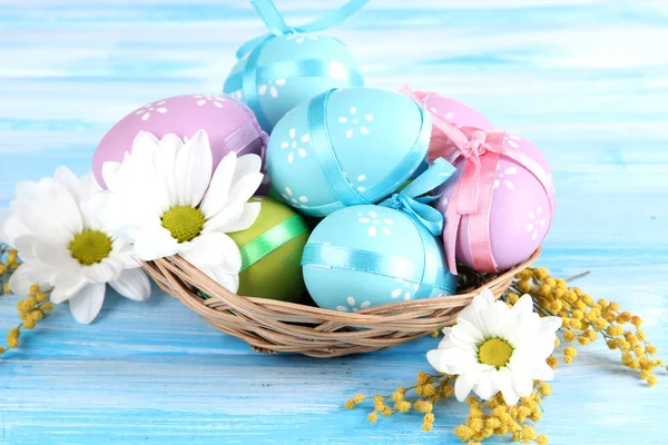 Easter eggs in basket and mimosa flowers, on blue wooden background — Stock Photo, Image