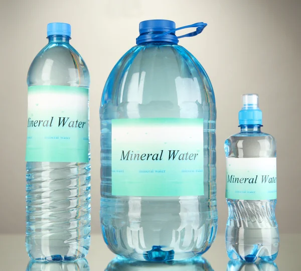 Different water bottles with label on grey background — Stock Photo, Image