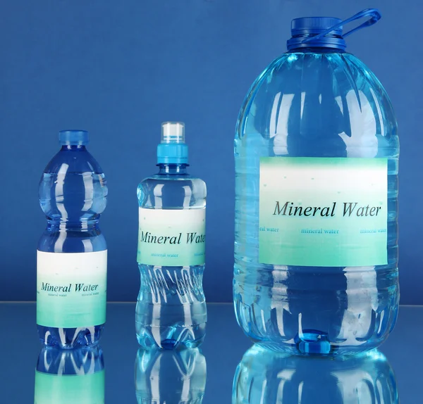 Diferentes botellas de agua con etiqueta sobre fondo azul — Foto de Stock