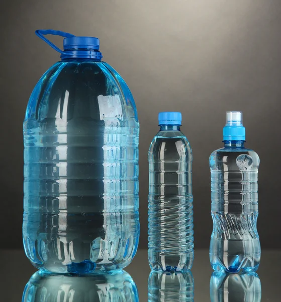 Různé lahve s vodou na šedém pozadí — Stock fotografie