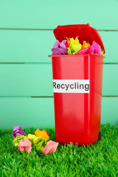Reciclagem bin com papéis na grama em fundo azul claro — Fotografia de Stock